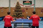 Lade das Bild in den Galerie-Viewer, Tischtennis Platte zwei junge Spieler T Shirt rot von Butterfly auf dem Rüscken MTV Soltau  mit Tischtennis Schläger spielend im Hintergrund Weihnachtsbaum mit Aufschrift Frohe Weihnachten wünscht MTV Soltau 
