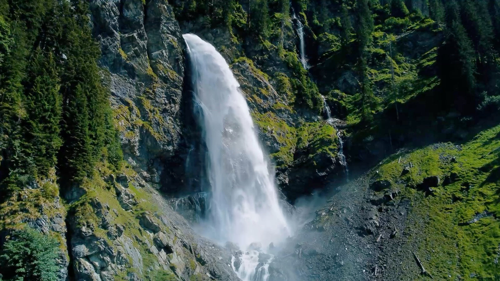 Wasserfall stürzt über eine bewachsene Felswand in einem Bergtal